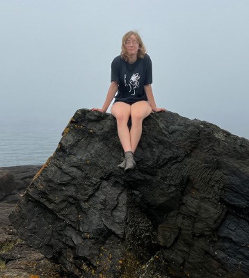 artist sitting on a rock with lake in background