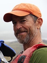 A portrait of a man in a life jacket with an orange hat on. A foggy background.