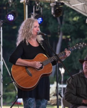 A woman holds a guitar and sings into a microphone