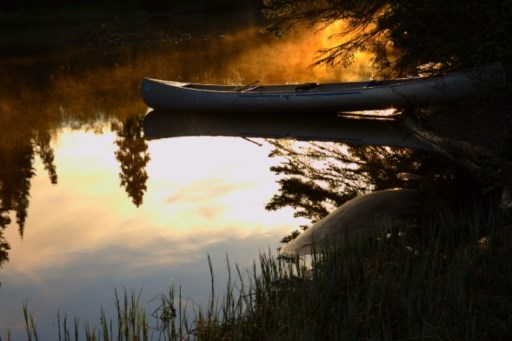 A canoe rests on shore with sun reflecting off the water