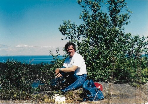 A photo shows a man taking a break from hiking with a scenic view in the background
