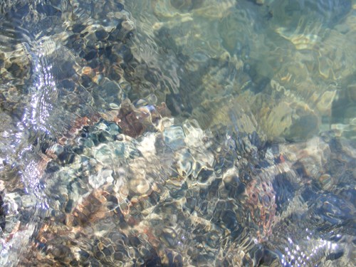 A photograph shows an abstract view of the surface of the water. You can see through down to lighter rocks beneath