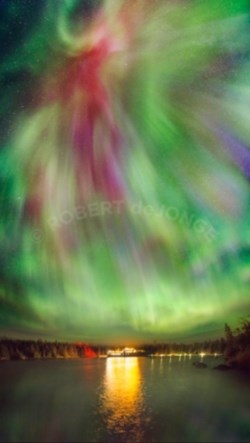 A lake scene with a large ferry on the bottom third of image, with northern lights in green and pink on the top two thirds. The ferry's light reflects off the water.