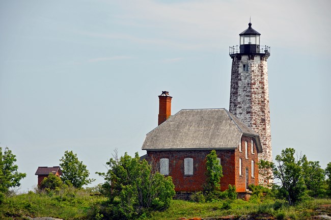 A tall white brick lighthouse next to red brick keeper's quarters.