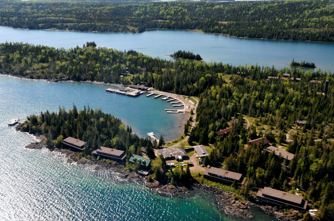 An aerial view of a lakeside harbor, lined with brown buildings, docks, and a marina.