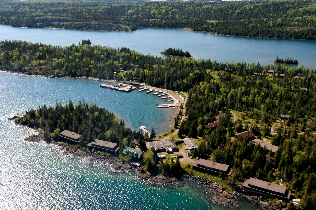An aerial view of a lakeside harbor, lined with brown buildings, docks, and a marina.