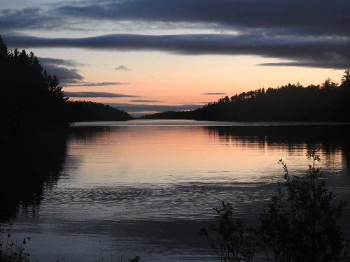 View of an orange and blue sunset over Lake Superior with trees silhouetted in the background.
