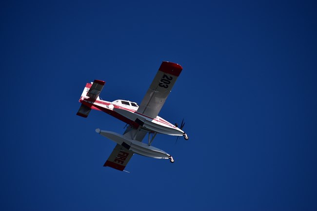 A white and yellow single engine airtanker (SEAT) flies in the sky.