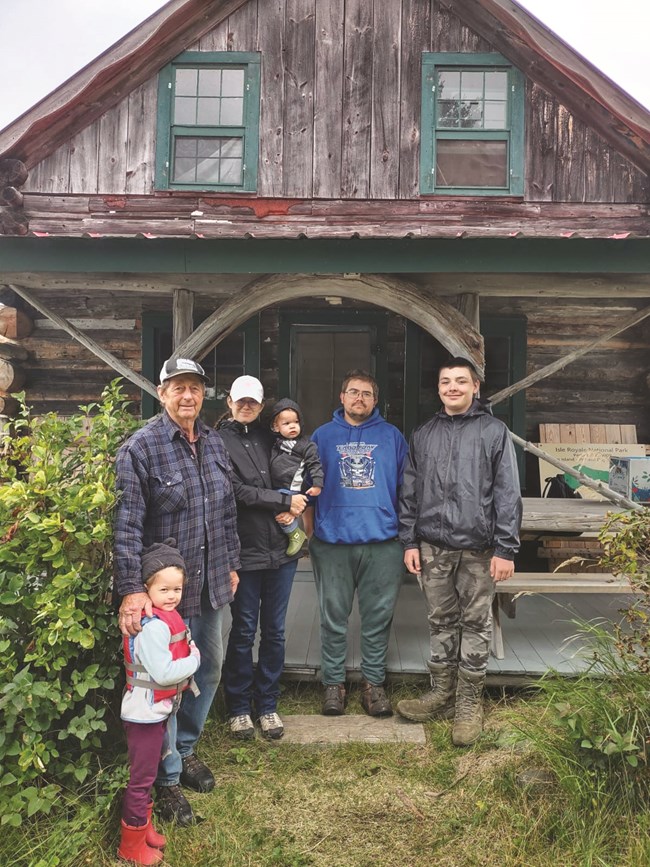 Four adults and two children pose for a photo in front of a historic structure.