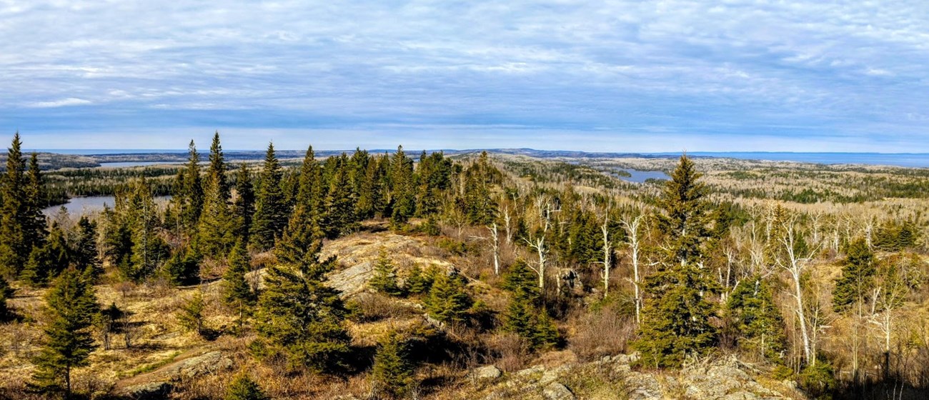 A landscape photo featuring rocky ridges, multiple lakes, and a large forest, with blue skies in the background.