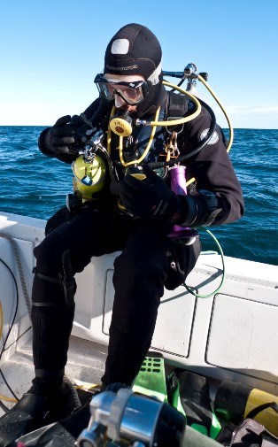 A diver in full scuba gear sits on the side of a boat, preparing for a dive.