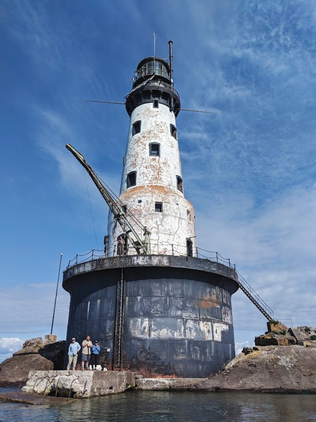 Three people standing at the base of a tall, white lighthouse.
