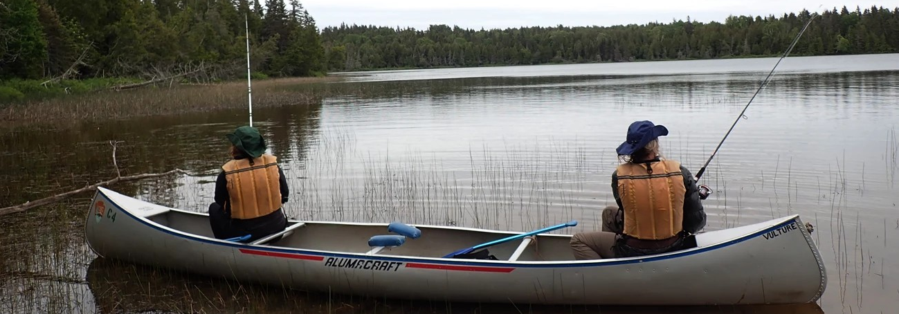 Two people fish from a canoe on an interior lake.