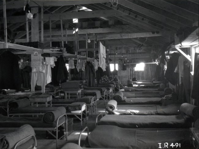 interior of barracks building with beds neatly made and clothes neatly hung