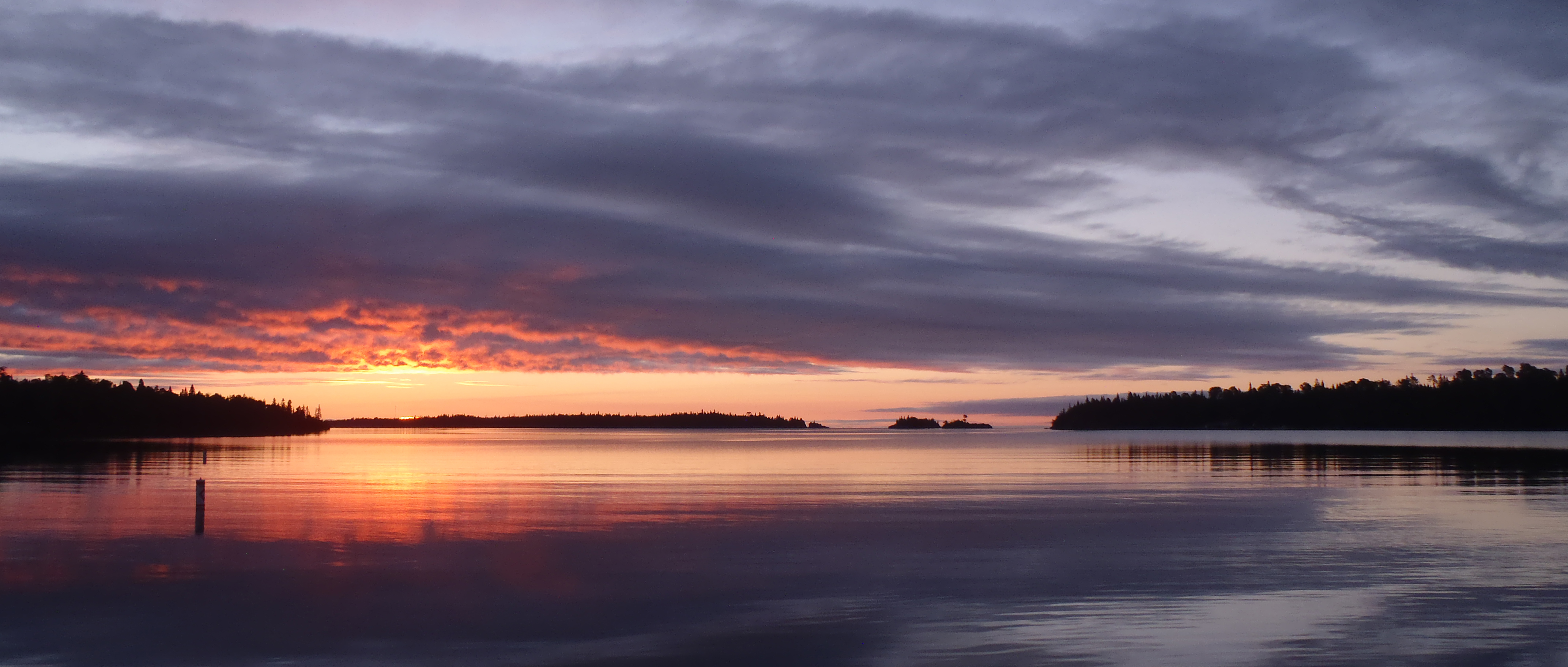 A yellow, pink and orange scenic sun rising over a deep purple lake.