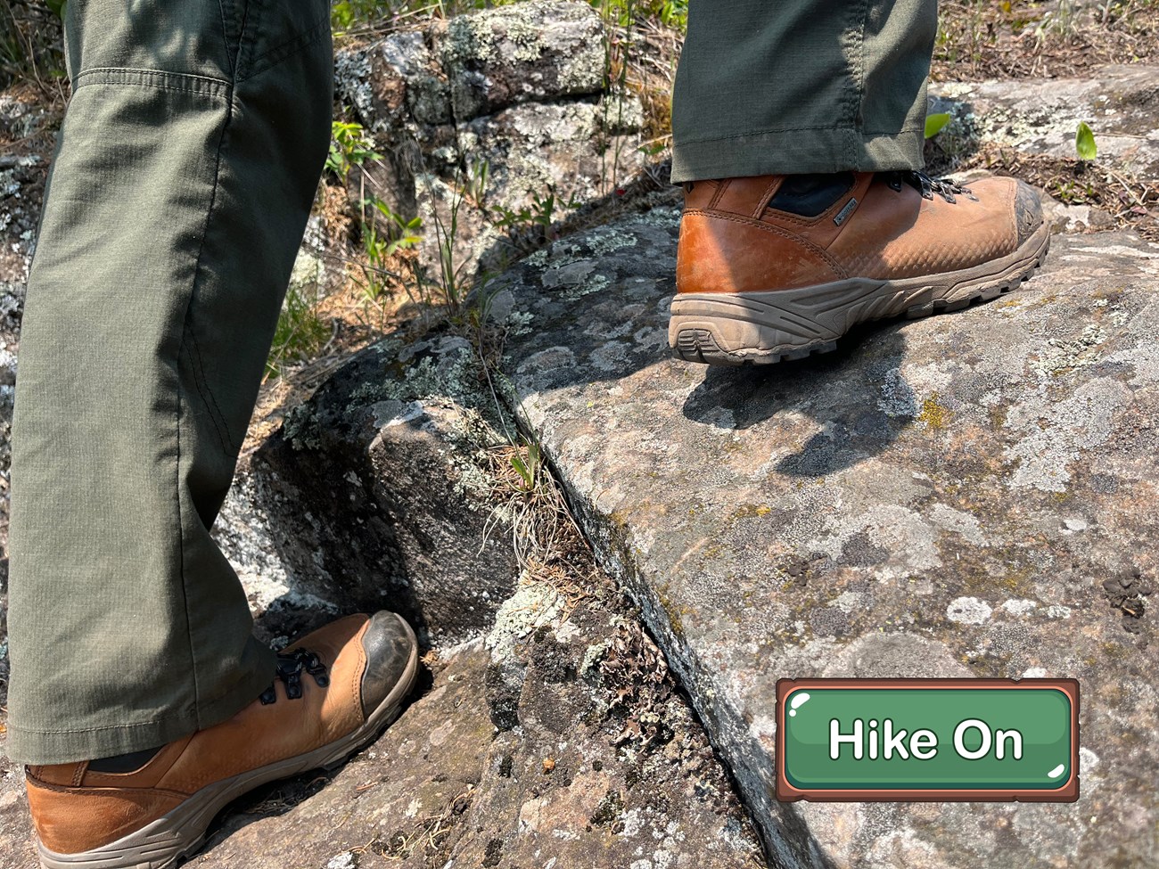 Close up of a person's feet in brown hiking boots hiking up some rocks.