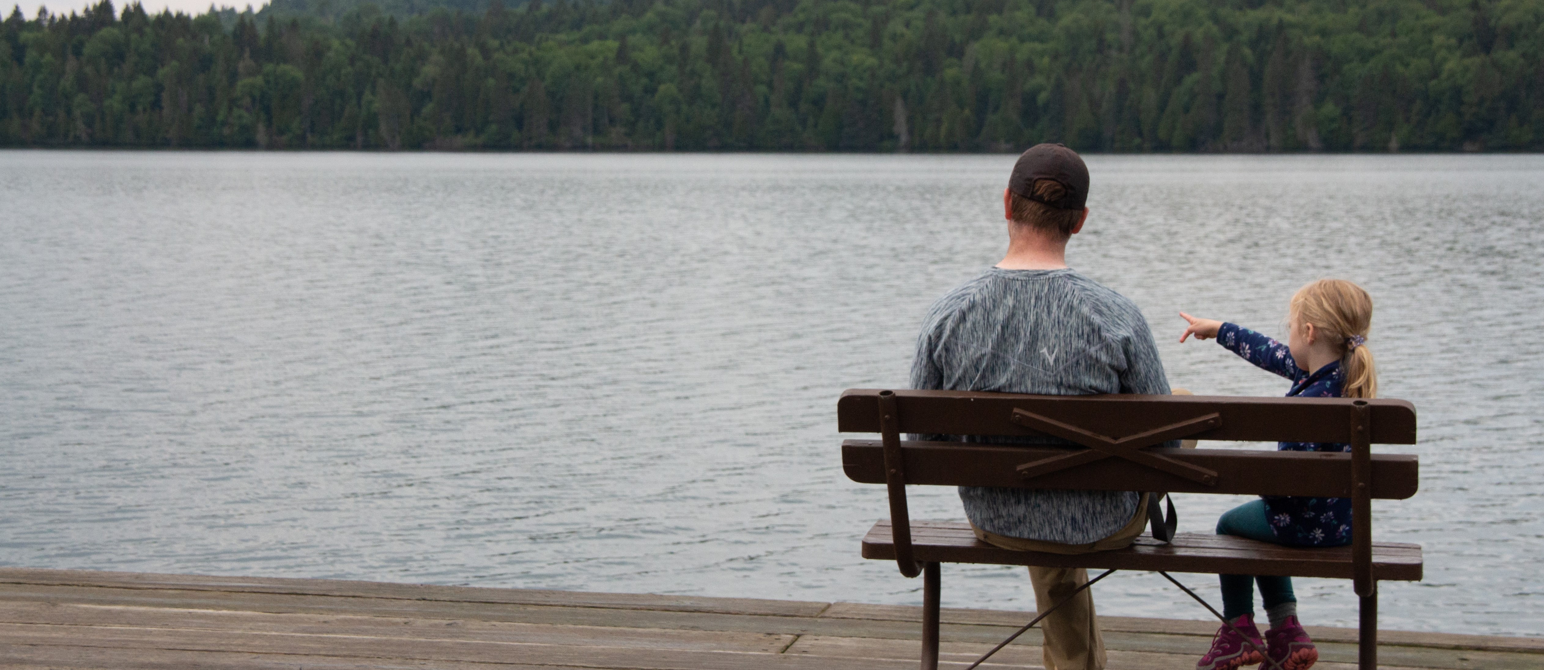Father and young daughter sitting on a bench looking out into the harbor.