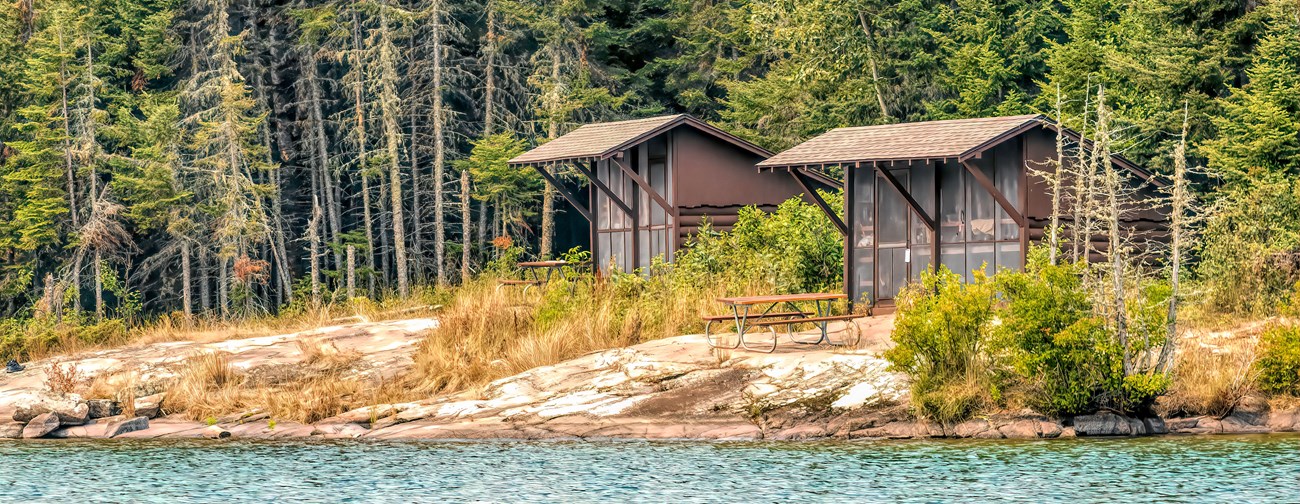 Wooden camp shelters near a lake.