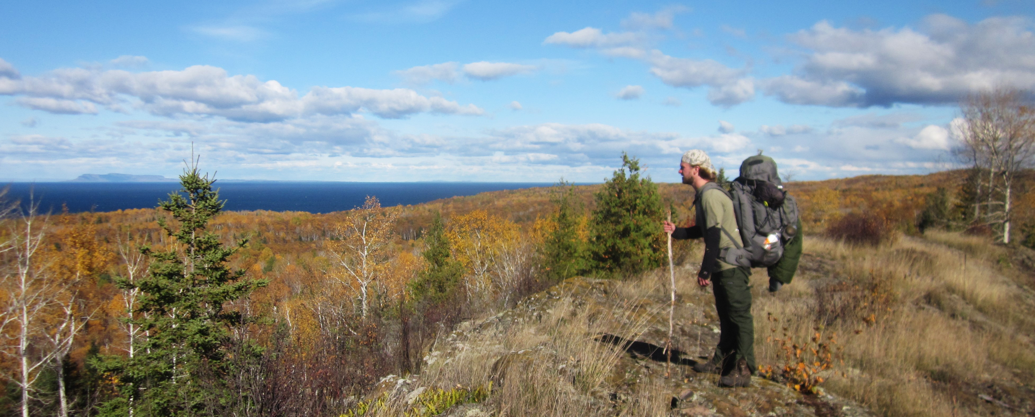 A person wearing a large backpack stands on a rocky ridge looking over a large overlook.
