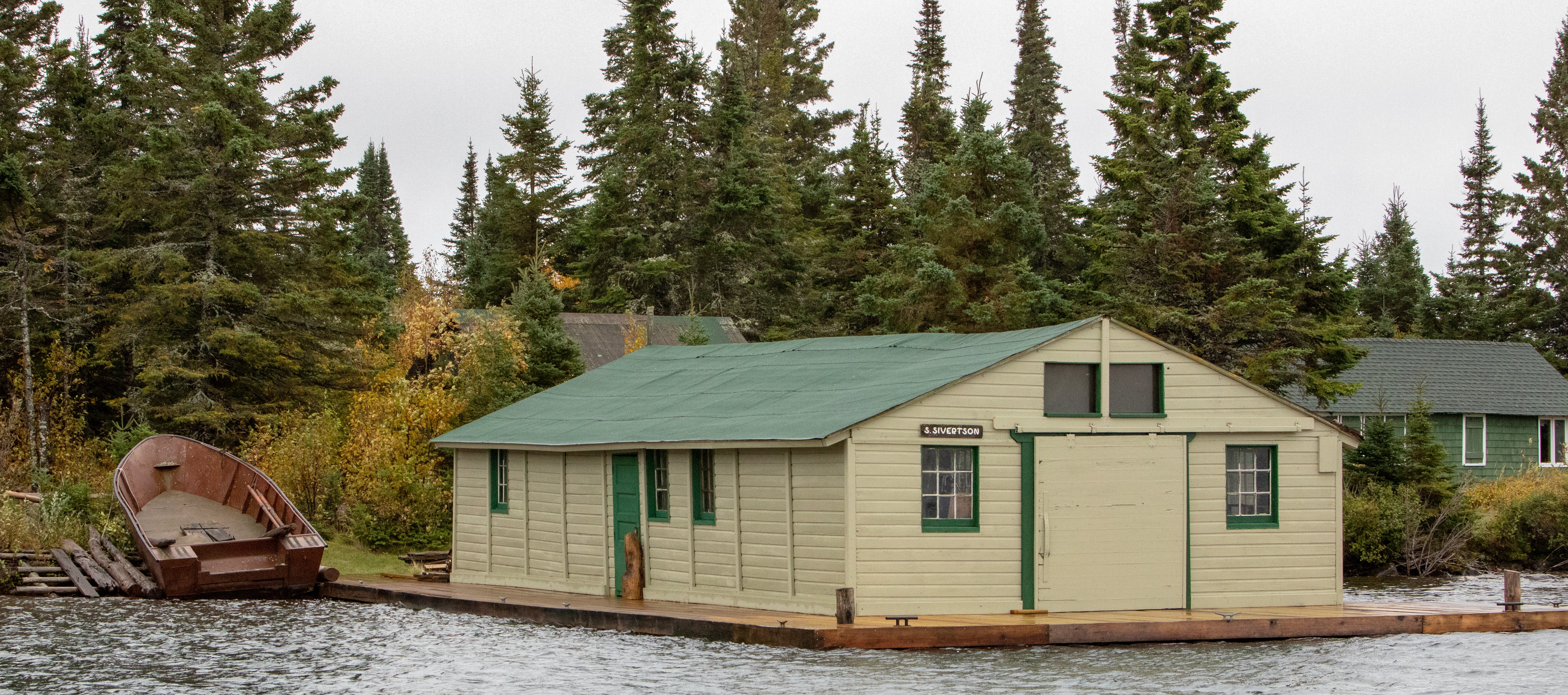 An old fishery with a tan building with a green roof on the water.