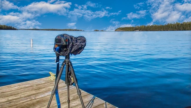A professional camera set up on a tripod on a wooden dock, aimed at Lake Superior.