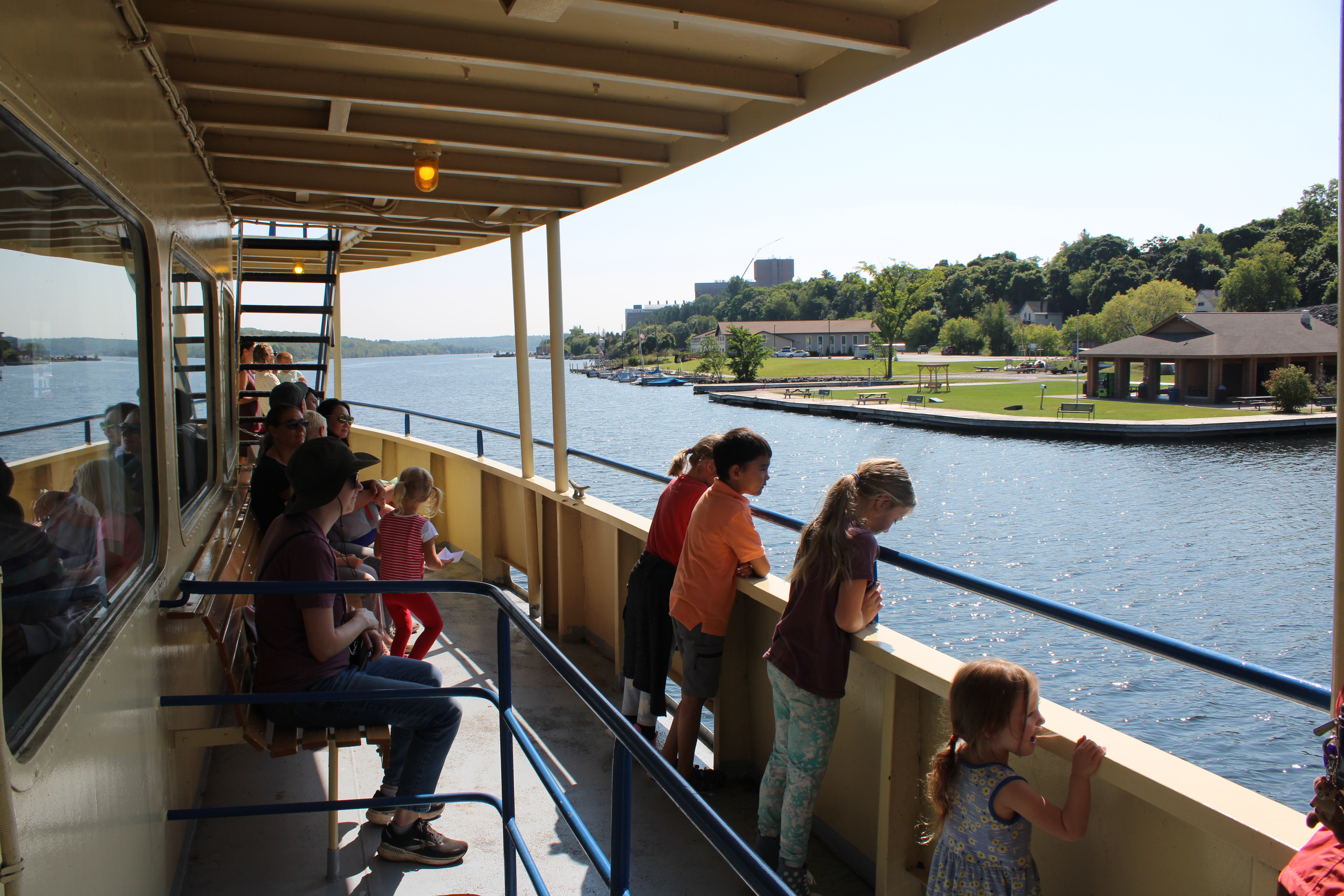 Multiple children on the upper deck of a ferry looking at the water.