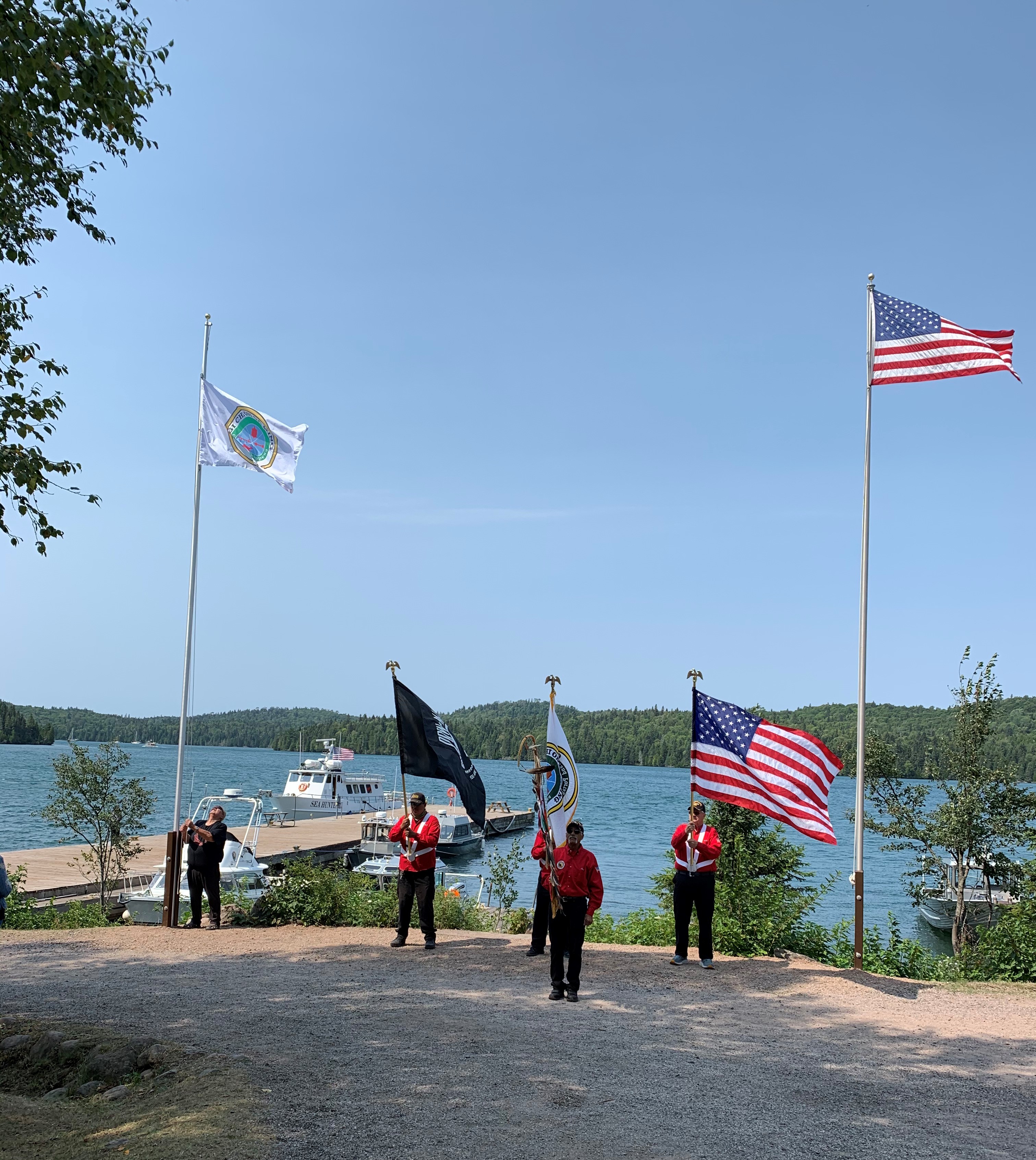 ISRO_Band-Flag-Going-Up-at-Windigo-2021 A small group of people stand beneath two flag poles.