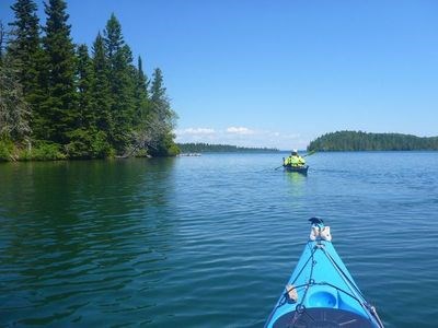 Two kayakers paddle along the treelined shoreline of Isle Royale.