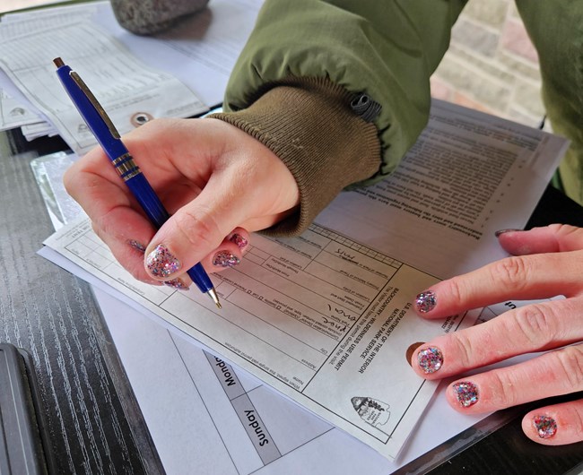 Close up of hands holding a pen filling out a small white piece of paper.