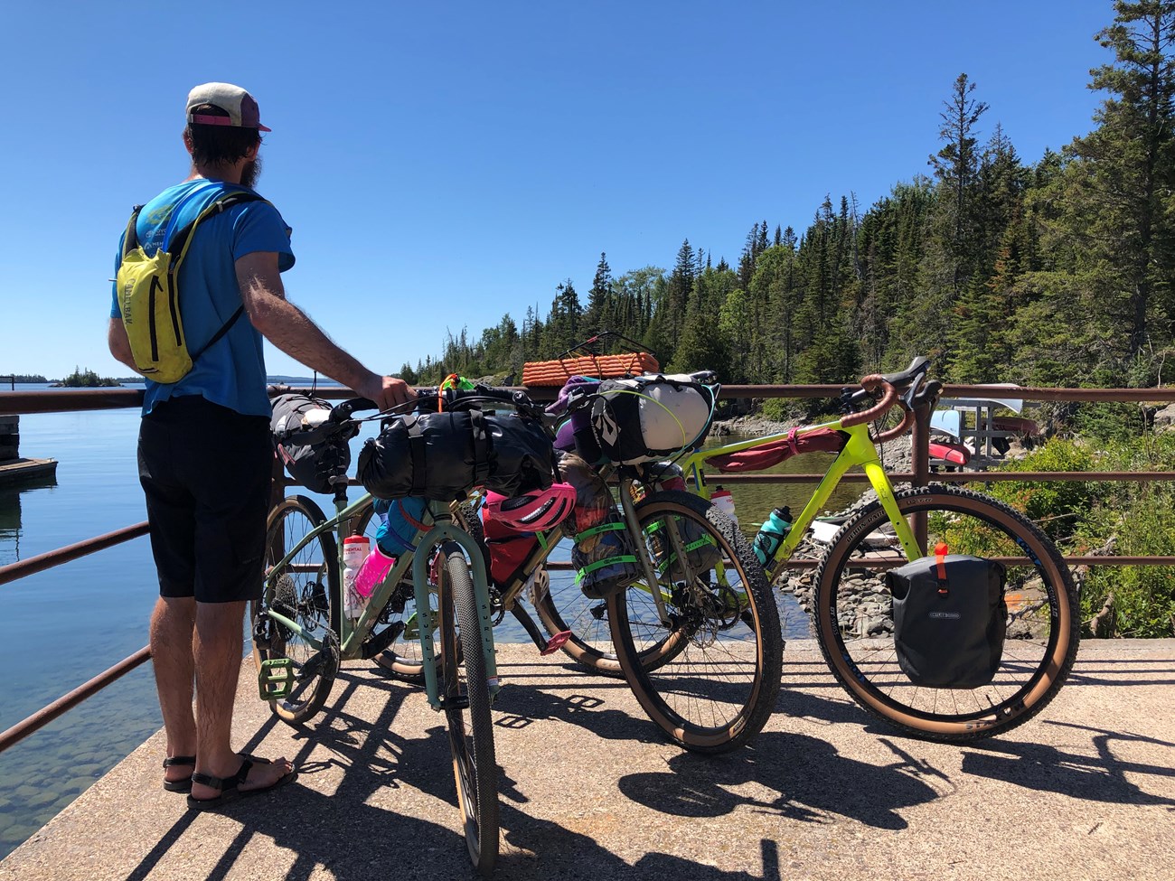A person stands next to three bicycles loaded with gear while looking out to Lake Superior.