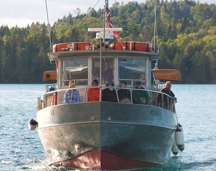 The Voyageur II passenger vessel as seen from the bow sailing for Isle Royale. Passengers sit along the bow cabin windows. The Voyageur II passenger vessel as seen from the bow sailing for Isle Royale. Passengers sit along the bow cabin windows.