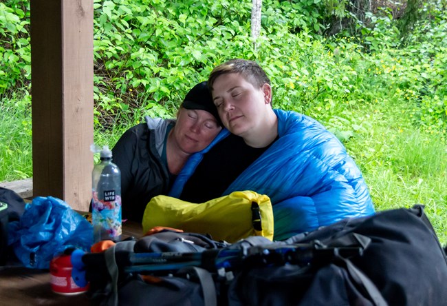 Two people rest while wrapped in a camp blanket.