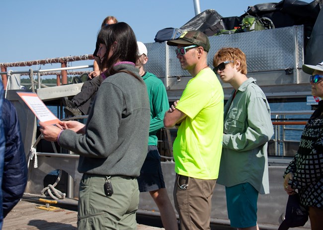 A person reads a cue card while standing on a dock next to a passenger ferry.