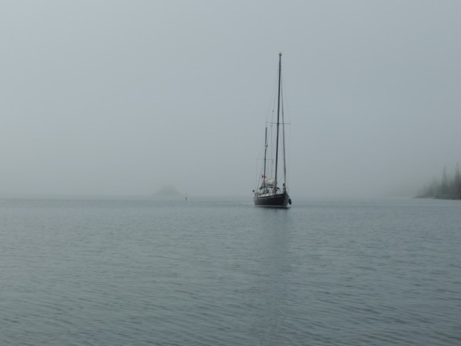 A sailboat flying a Canadian flag arrives at Isle Royale in foggy weather conditions.