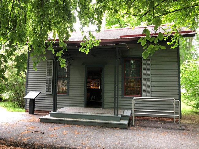 a small gray building with a red roof that has a porch