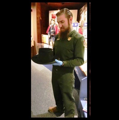 man in a National Park Service uniform is holding a black felt top hat