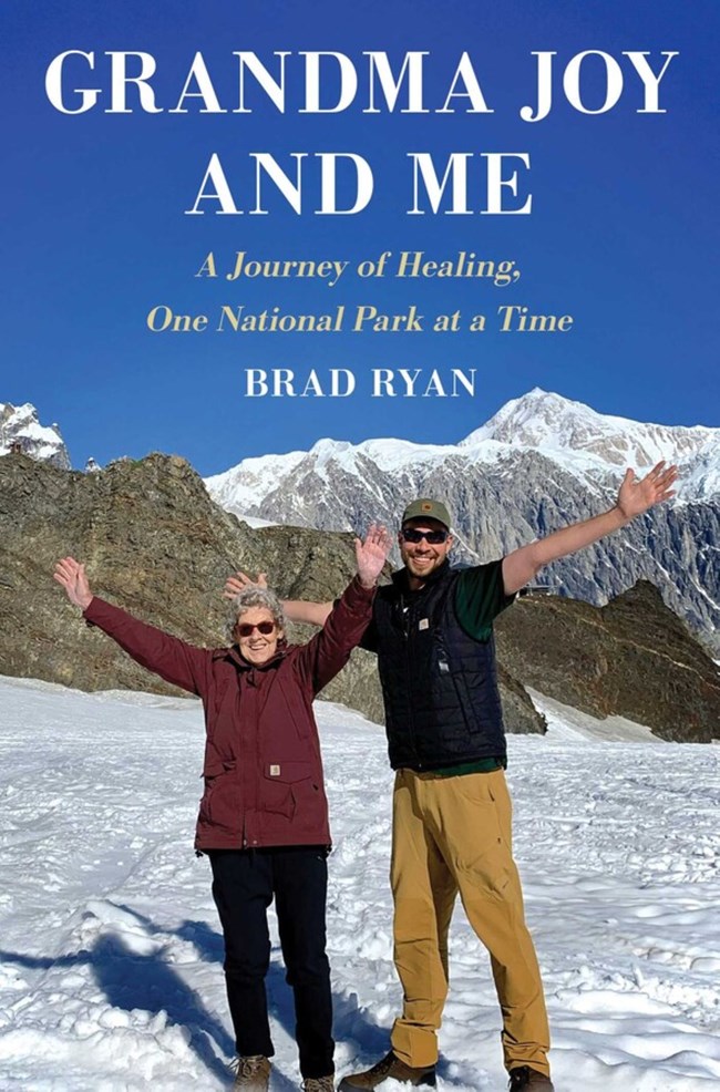 Young man and his grandmother standing with arms outstretched in front of a mountain range