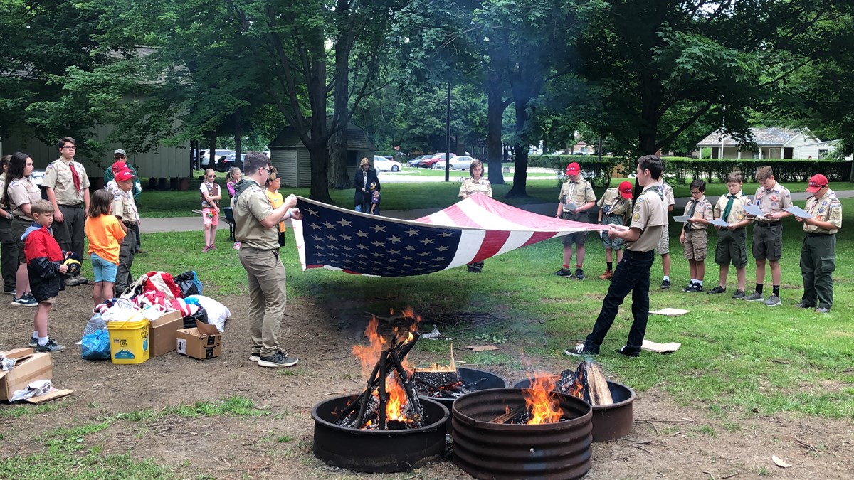 people holding flag approaching a barrel with a fire.