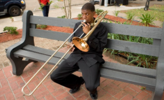 Young man seated on park bench playing trombone.