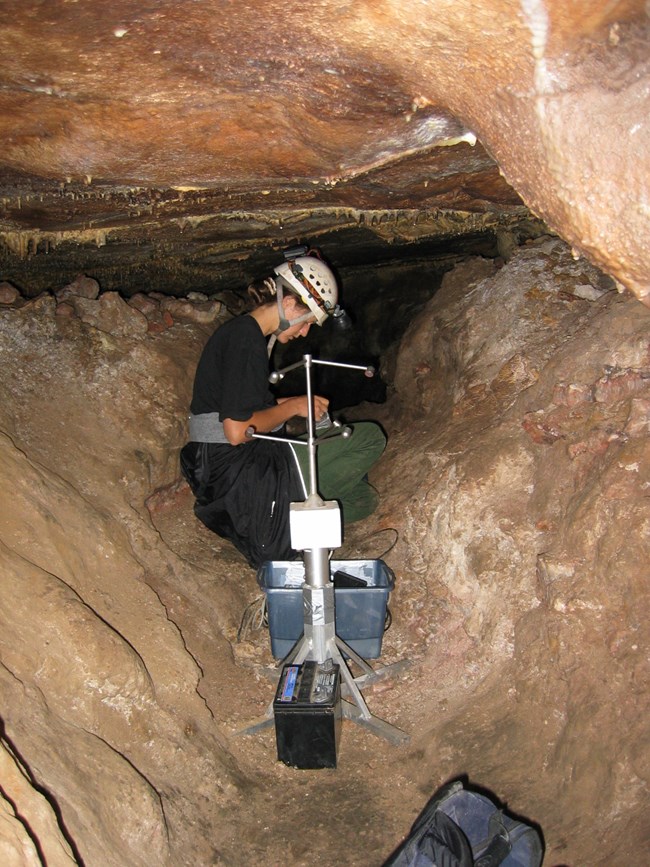 A caver is kneeling in a passageway, writing data into a small book.