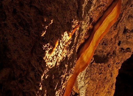 A calcite strand discolored reds, oranges, and yellows, similar to bacon, adorns the cave wall.