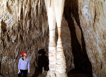 A cave explorer stands beside a pilar of calcite that is twice as tall as them.