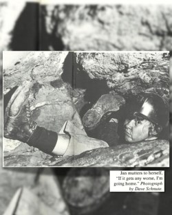 A woman makes her way through a tight squeeze in a cave. Her feet right next to her head, and a carbide lantern on her helmet. Photo description in the bottom right corner reading “Jan mutters to herself “if it gets any worse. I’m going home.” Photograph