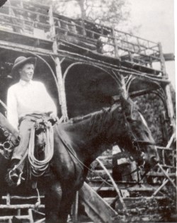 [alt text- One of the Michaud's rides on a horse with their 2-story log cabin in the background.]