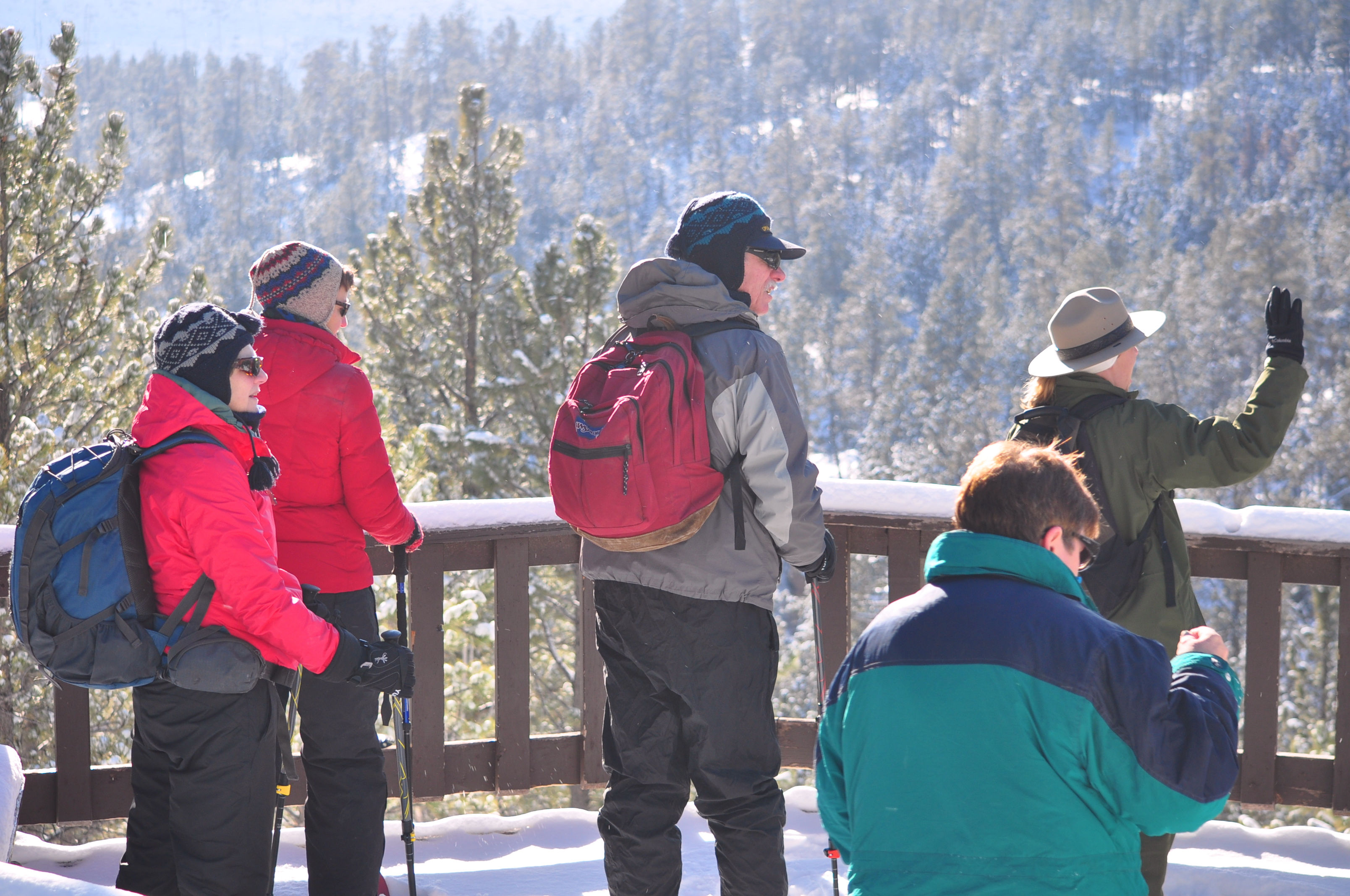 Snowshoe participants stand on an observation deck and listen to a park ranger.