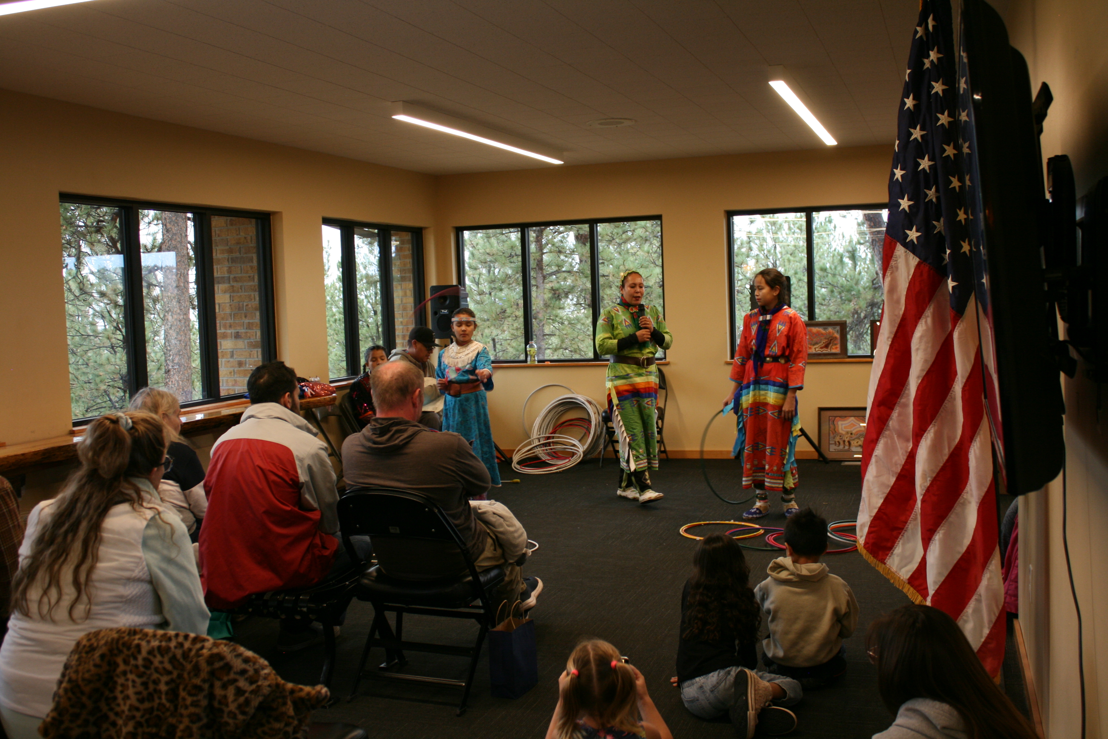 Three people stand at the front of a room with a seating audience watching.