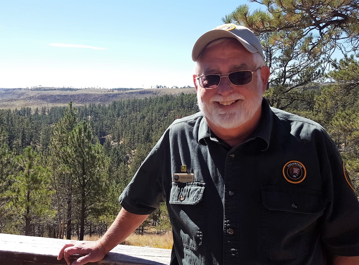 Volunteer smiling in front of pine tree vista Volunteer smiling in front of pine tree vista