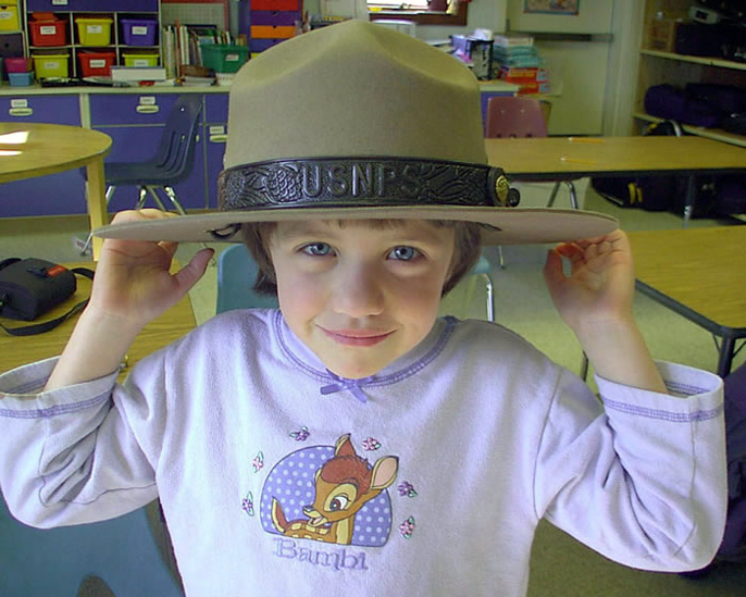 An elementary school student tries on a park ranger hat.