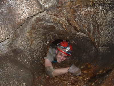 A caver squeezes through a small opening known as Hurricane Corner on the Wild Caving Tour route in Jewel Cave.