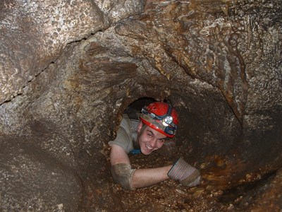 A caver squeezes through a small opening known as Hurricane Corner on the Wild Caving Tour route in Jewel Cave. A caver squeezes through a small opening known as Hurricane Corner on the Wild Caving Tour route in Jewel Cave.